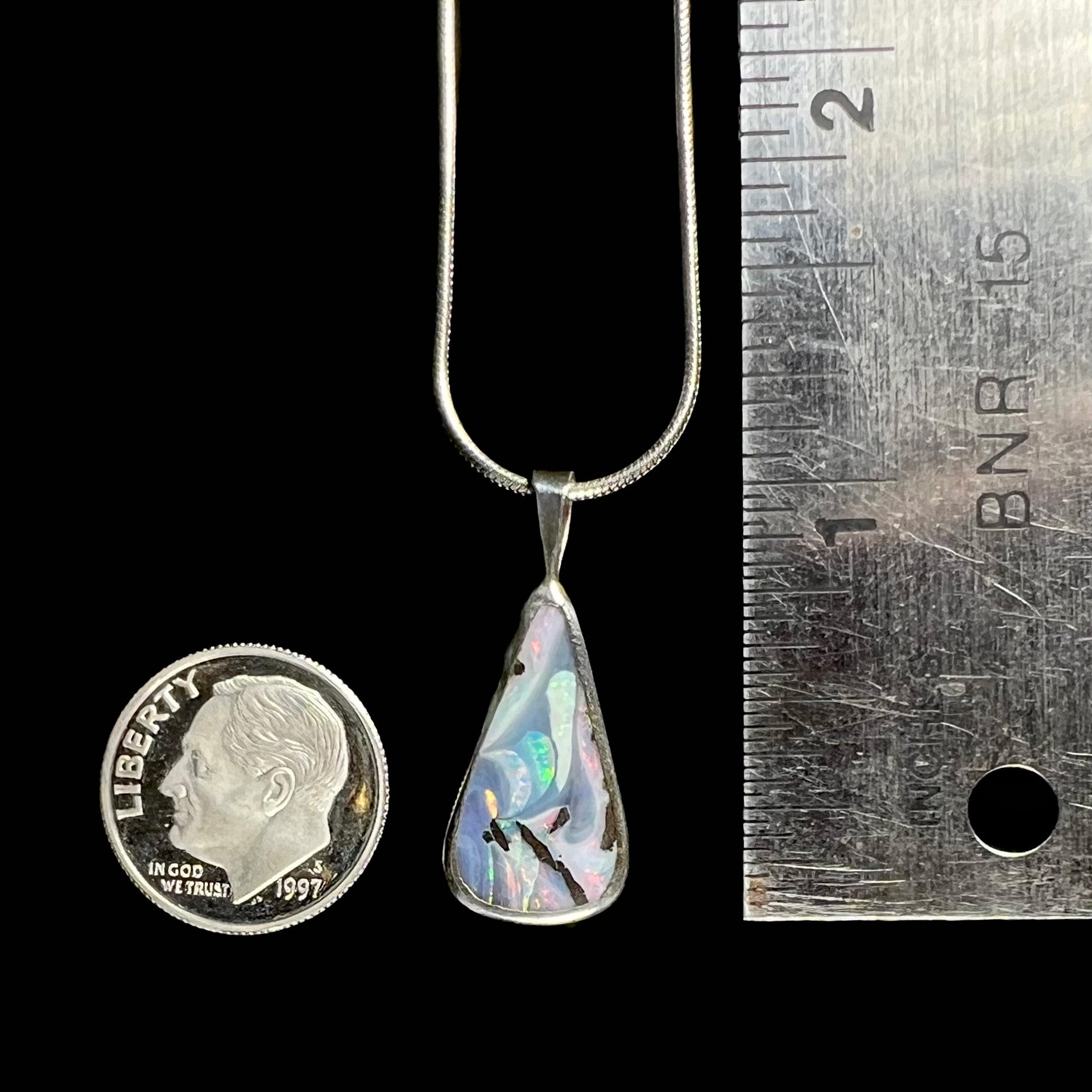 A boulder opal necklace next to a dime and ruler for size comparison, measuring approximately 1 inch with the bail.