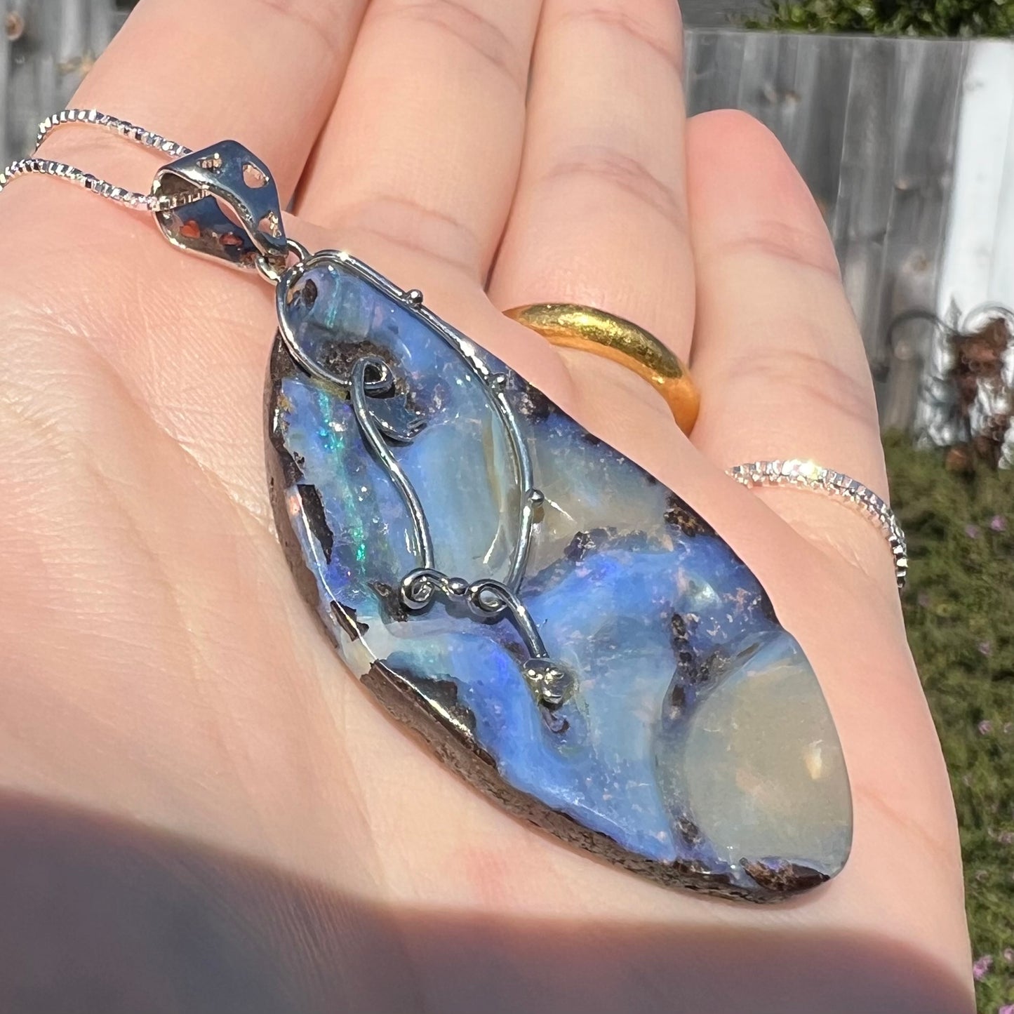 Angled view of a large, blue Australian boulder opal necklace in sterling silver, shown close-up in sunlight.