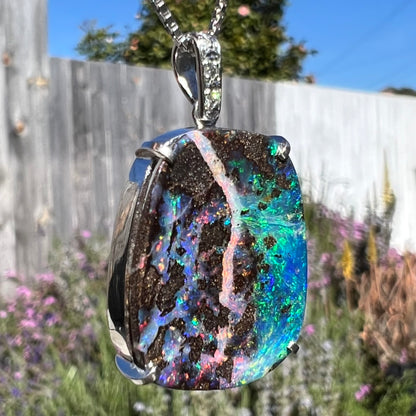 Macro shot of a boulder opal pendant in sunlight, highlighting the opal’s purple and pink hues.