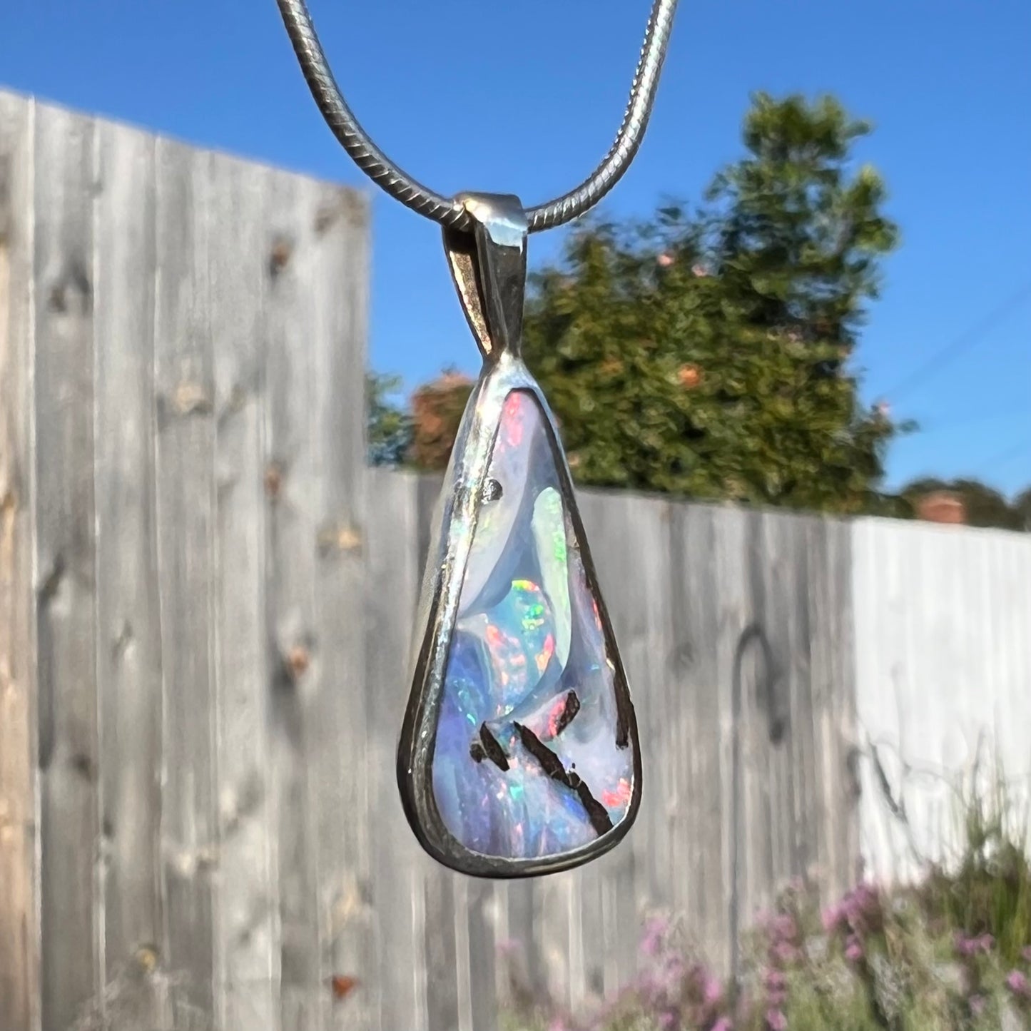 A macro view of a boulder opal necklace outdoors, twisted at an angle to highlight its swirling colors.