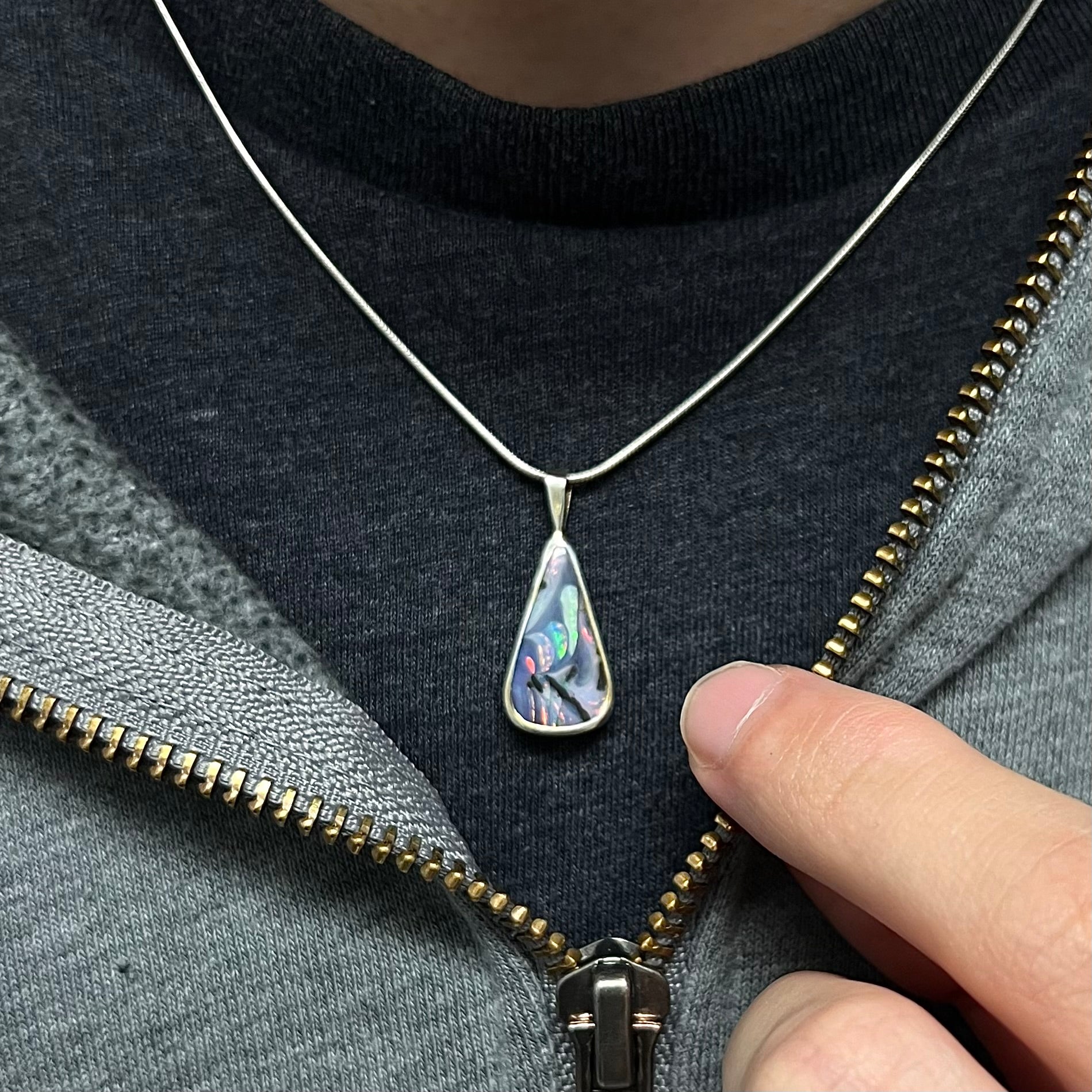 A boulder opal necklace worn around the neck on a black T-shirt, with its color play and pattern clearly visible.