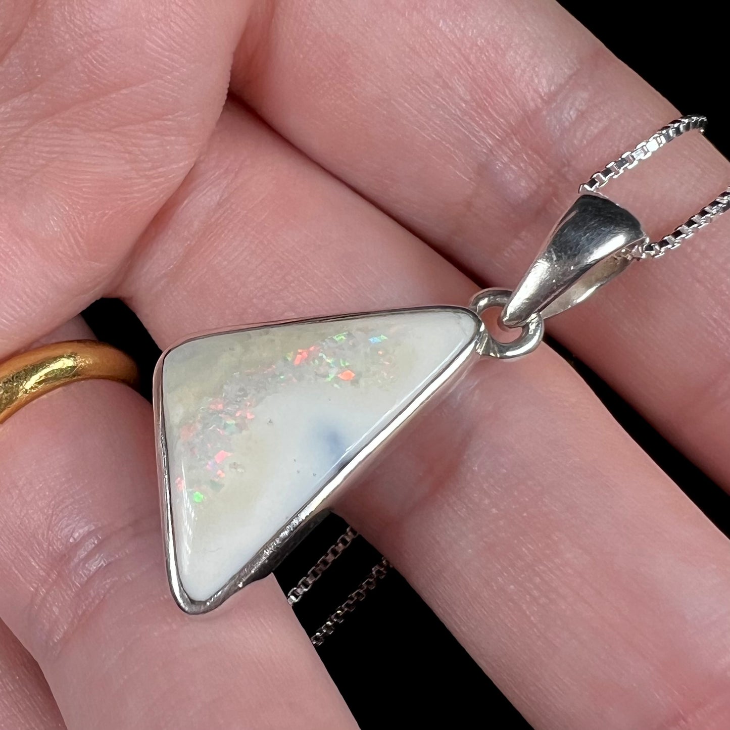 Angled close-up view of a white Australian boulder opal necklace in .950 silver, shown in a hand.
