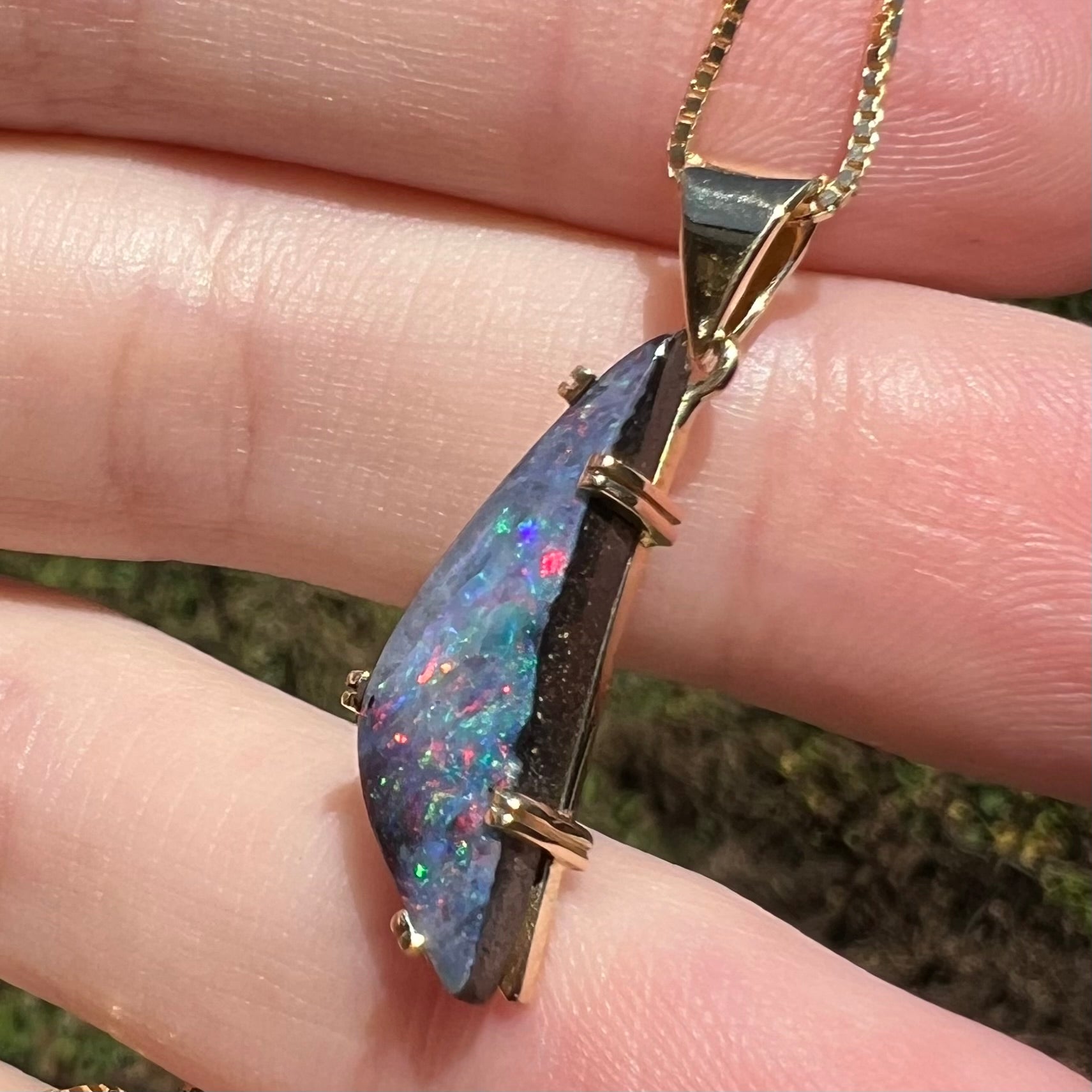 Close-up of Australian boulder opal pendant in 18k gold, held in hand in sunlight
