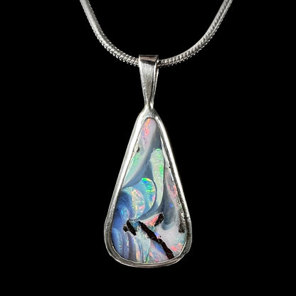 A boulder opal pendant in sterling silver displayed against a black background, showing its vibrant red and green color play.