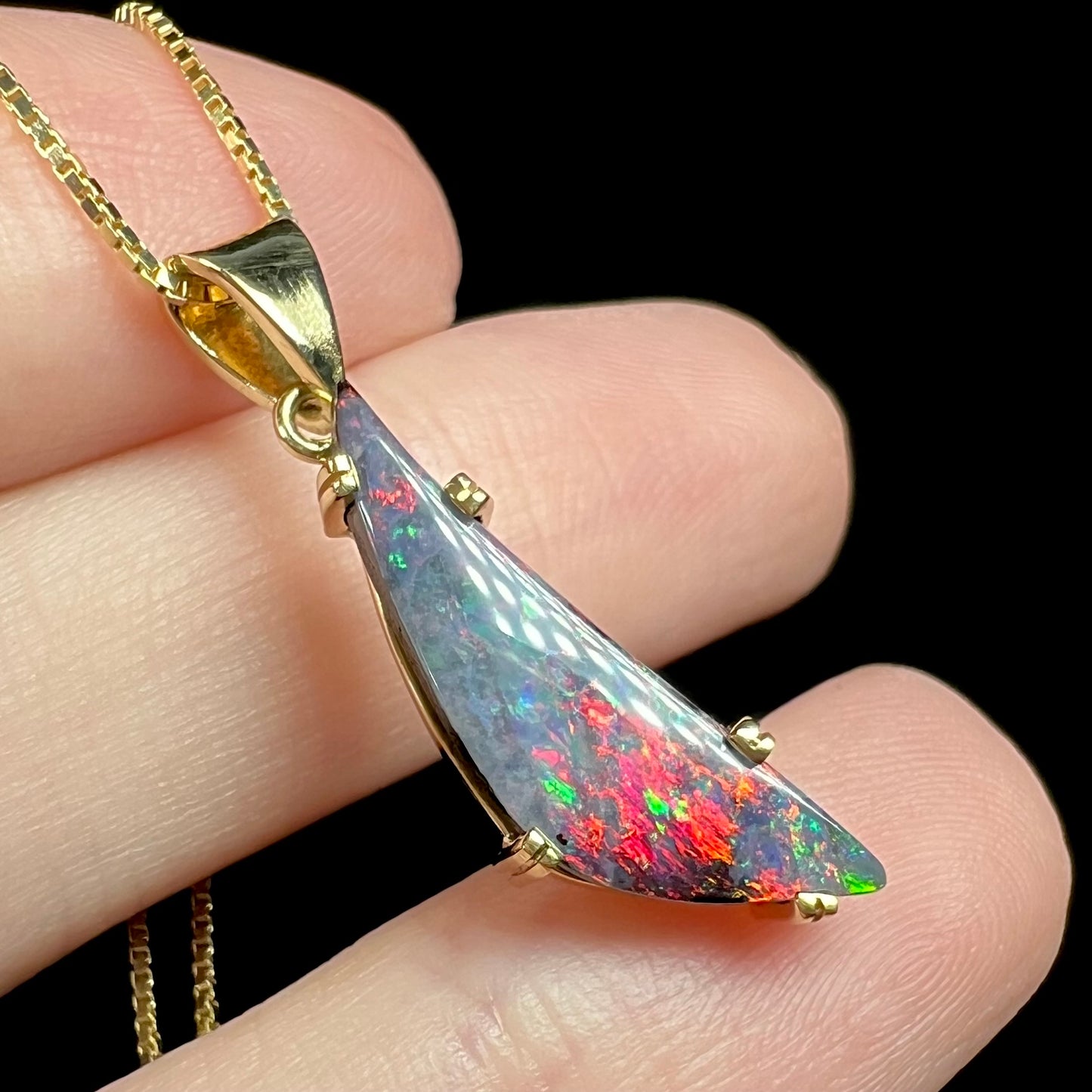 Bright red flashes seen in gold boulder opal pendant, held on top of fingers