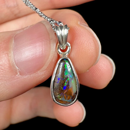 A natural, pear shaped Australian boulder opal with blue, purple, and green colors bezel set into a sterling silver necklace.