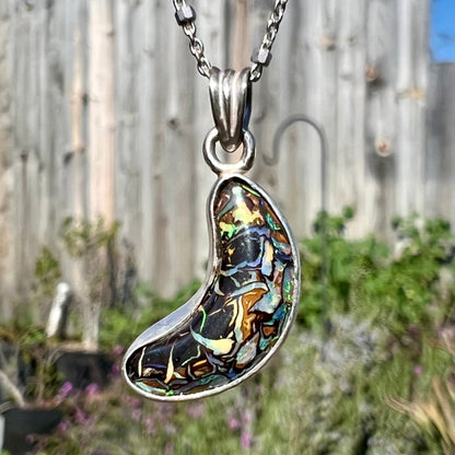 A sterling silver necklace set with a natural Koroit boulder opal shaped like a crescent moon.