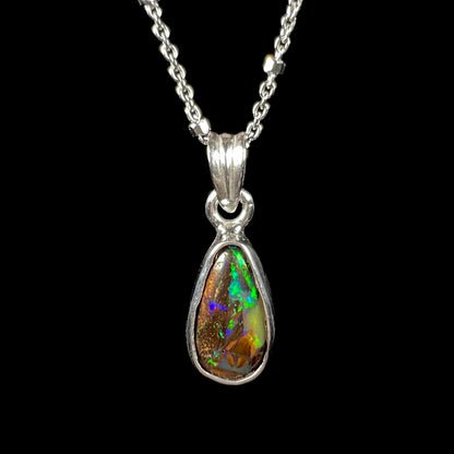 A natural, pear shaped Australian boulder opal with blue, purple, and green colors bezel set into a sterling silver necklace.