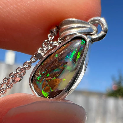 A pear shaped boulder opal necklace in sterling silver.  The opal has bright green and blue flashes.
