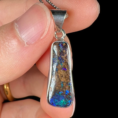 A sterling silver necklace bezel set with a natural Australian boulder opal stone.  The stone shines colors of blue, green, and purple.