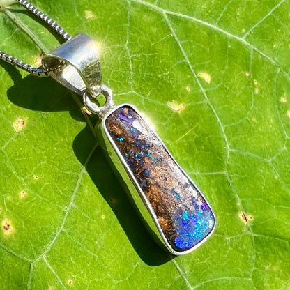 An elongated shaped natural boulder opal necklace in sterling silver.  The opal flashes bright blue and green colors.