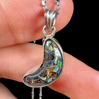 A sterling silver necklace bezel set with a natural Koroit boulder opal stone.  The stone is shaped like a crescent moon.