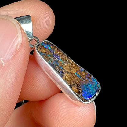 A sterling silver necklace bezel set with a natural Australian boulder opal stone.  The stone shines colors of blue, green, and purple.
