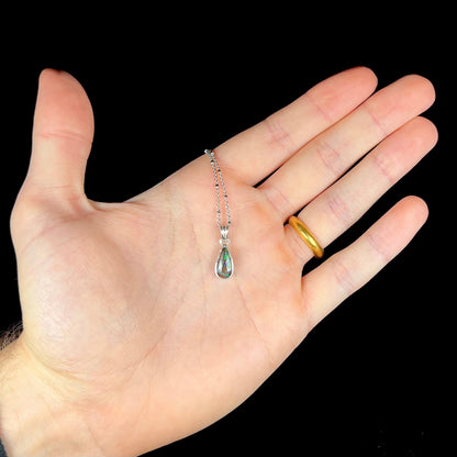 A natural, pear shaped Australian boulder opal with blue, purple, and green colors bezel set into a sterling silver necklace.