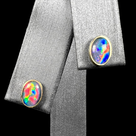 Pair of oval shaped opal triplet stud earrings in 9k gold with bright red and blue flashes of color, shown on earring display