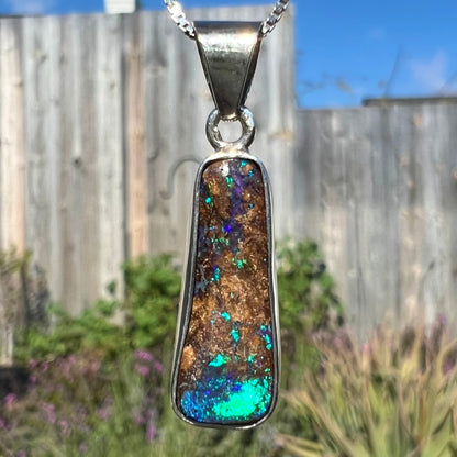 An elongated shaped natural boulder opal necklace in sterling silver.  The opal flashes bright blue and green colors.