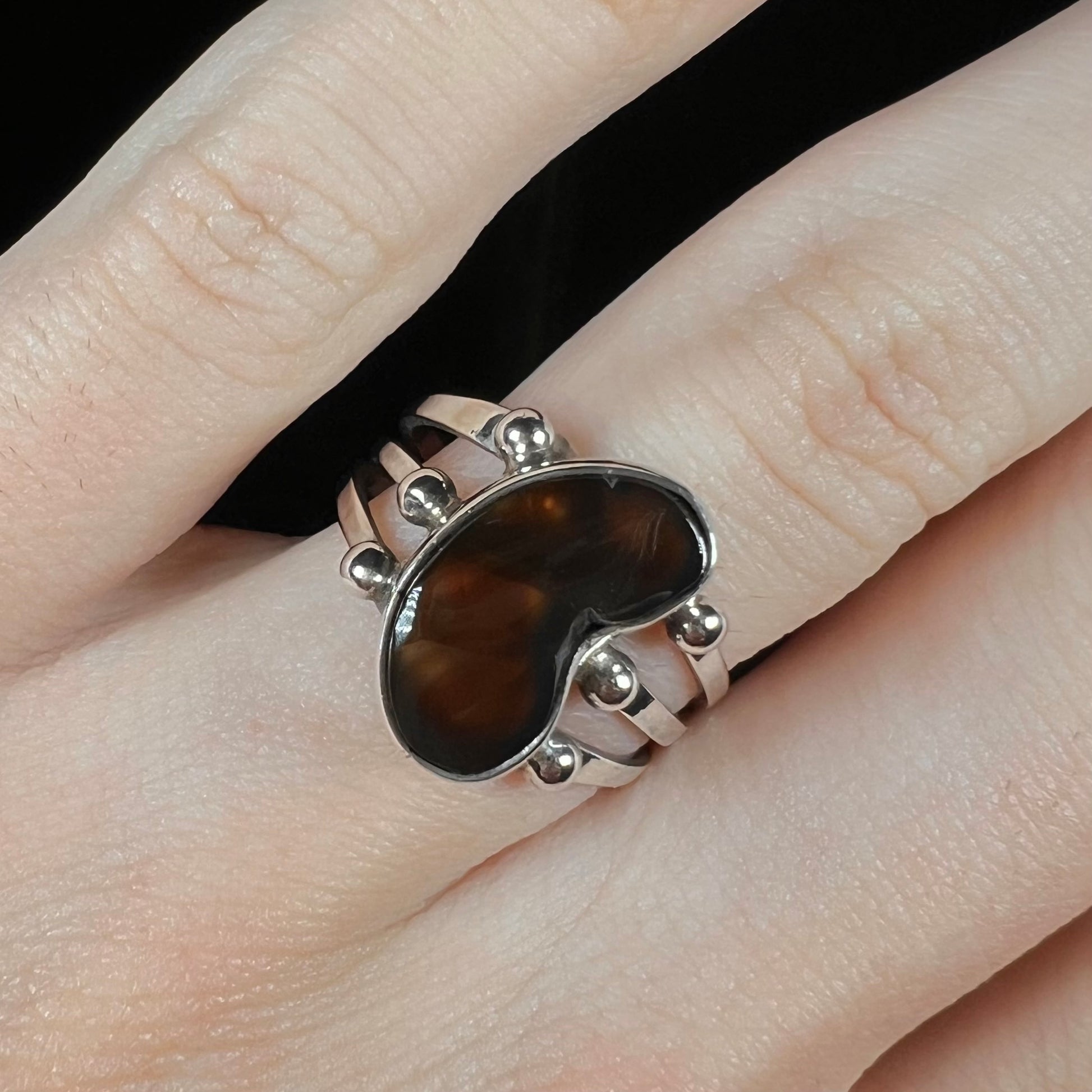 Close-up of brown fire agate ring on hand against black background.