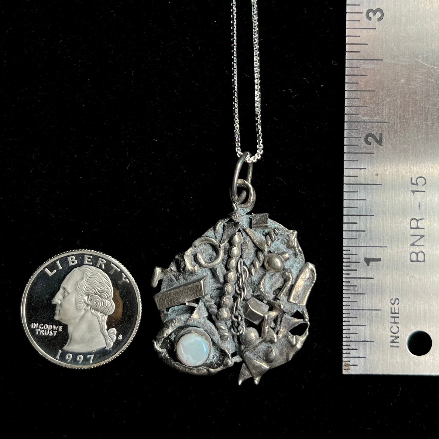 A brutalist silver opal necklace measuring 1.75 inches long shown next to a quarter and ruler.