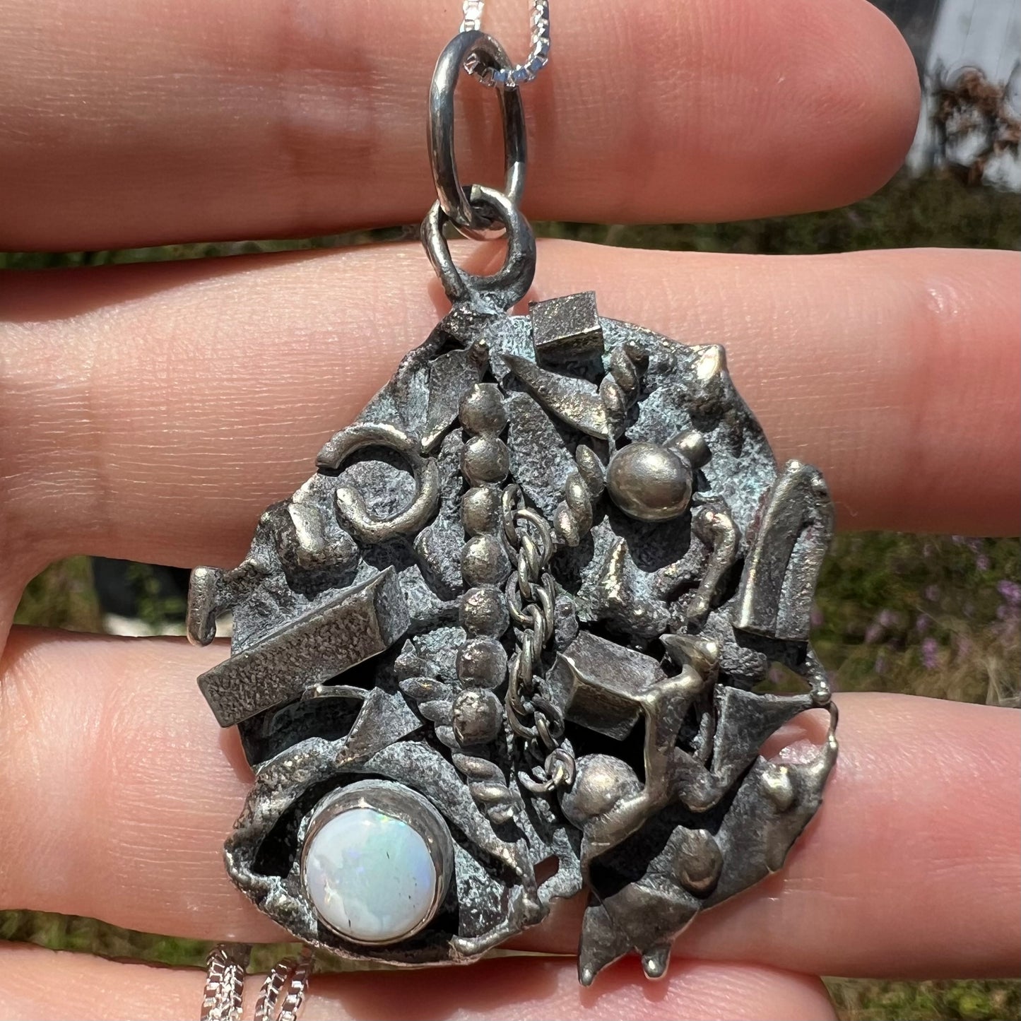 Close-up sunlit front view of a brutalist opal necklace made from sterling silver scrap metal.