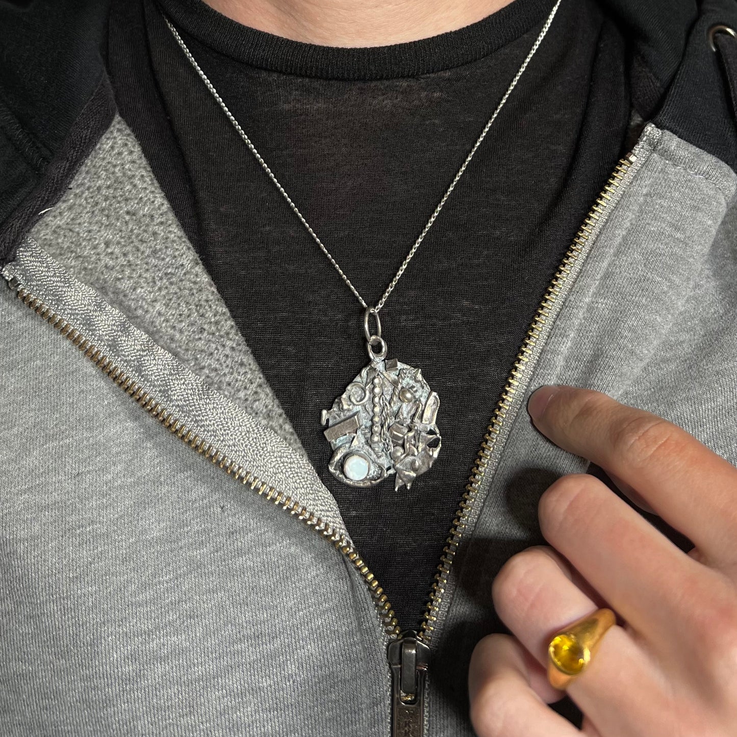 A brutalist opal necklace made from sterling silver scrap, worn around a neck against a dark shirt and hoodie.