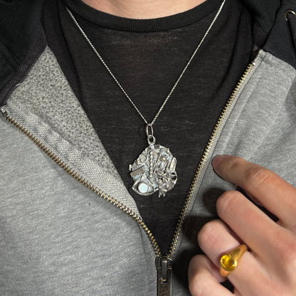 A brutalist opal necklace made from sterling silver scrap, worn around a neck against a dark shirt and hoodie.