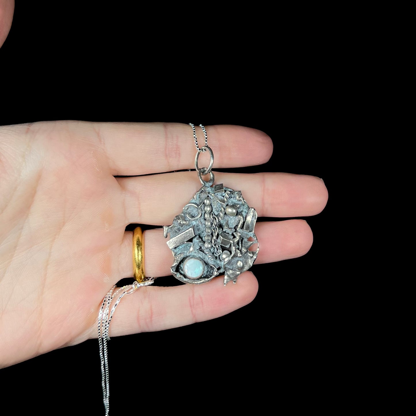 A sterling silver brutalist-style opal pendant held in a hand against a black background.