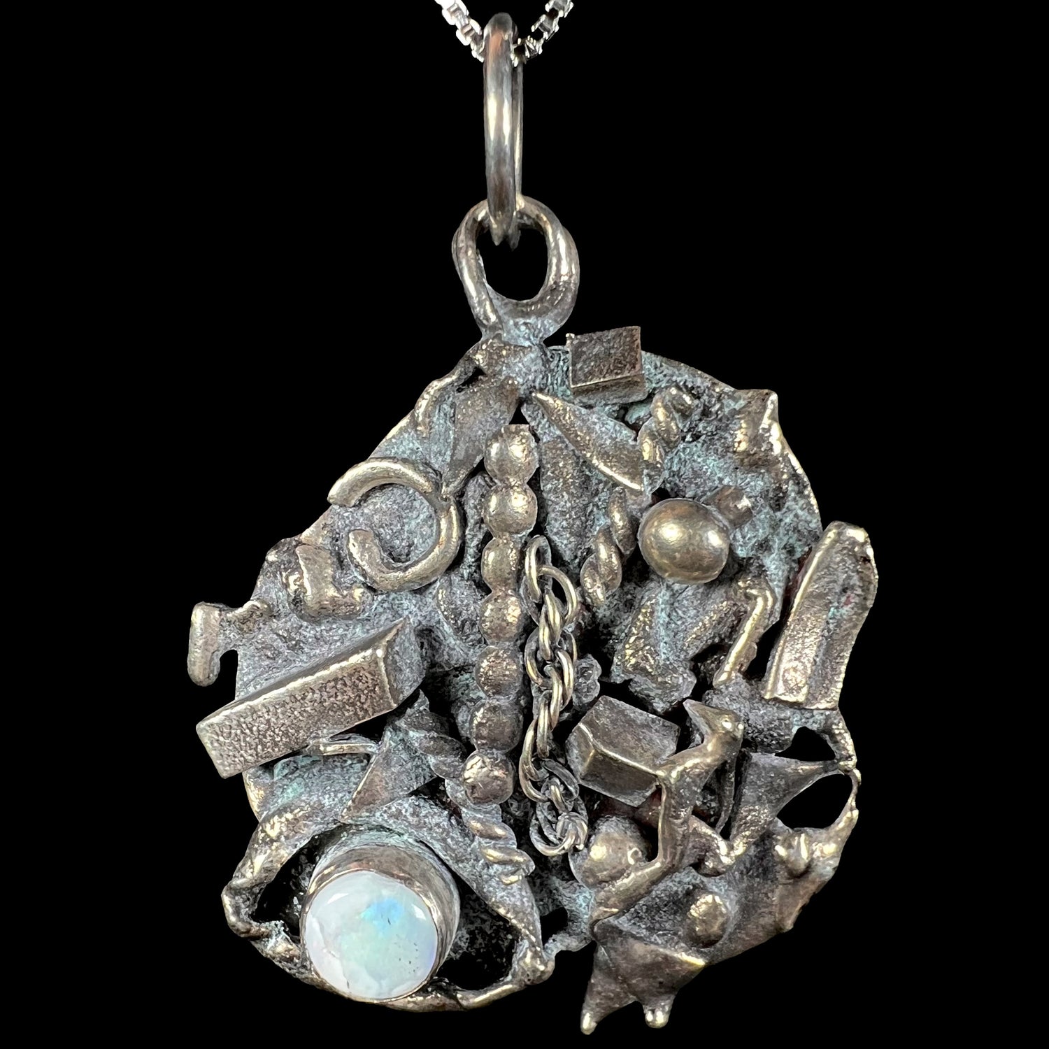 A brutalist opal pendant made from sterling silver scrap metal, depicting a shipwreck, shown from the front.