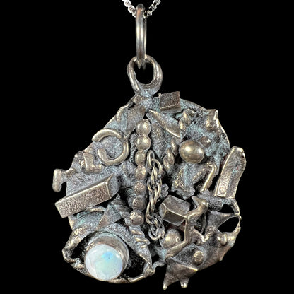 A brutalist opal pendant made from sterling silver scrap metal, depicting a shipwreck, shown from the front.