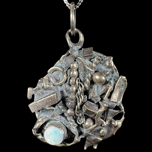 A brutalist opal pendant made from sterling silver scrap metal, depicting a shipwreck, shown from the front.
