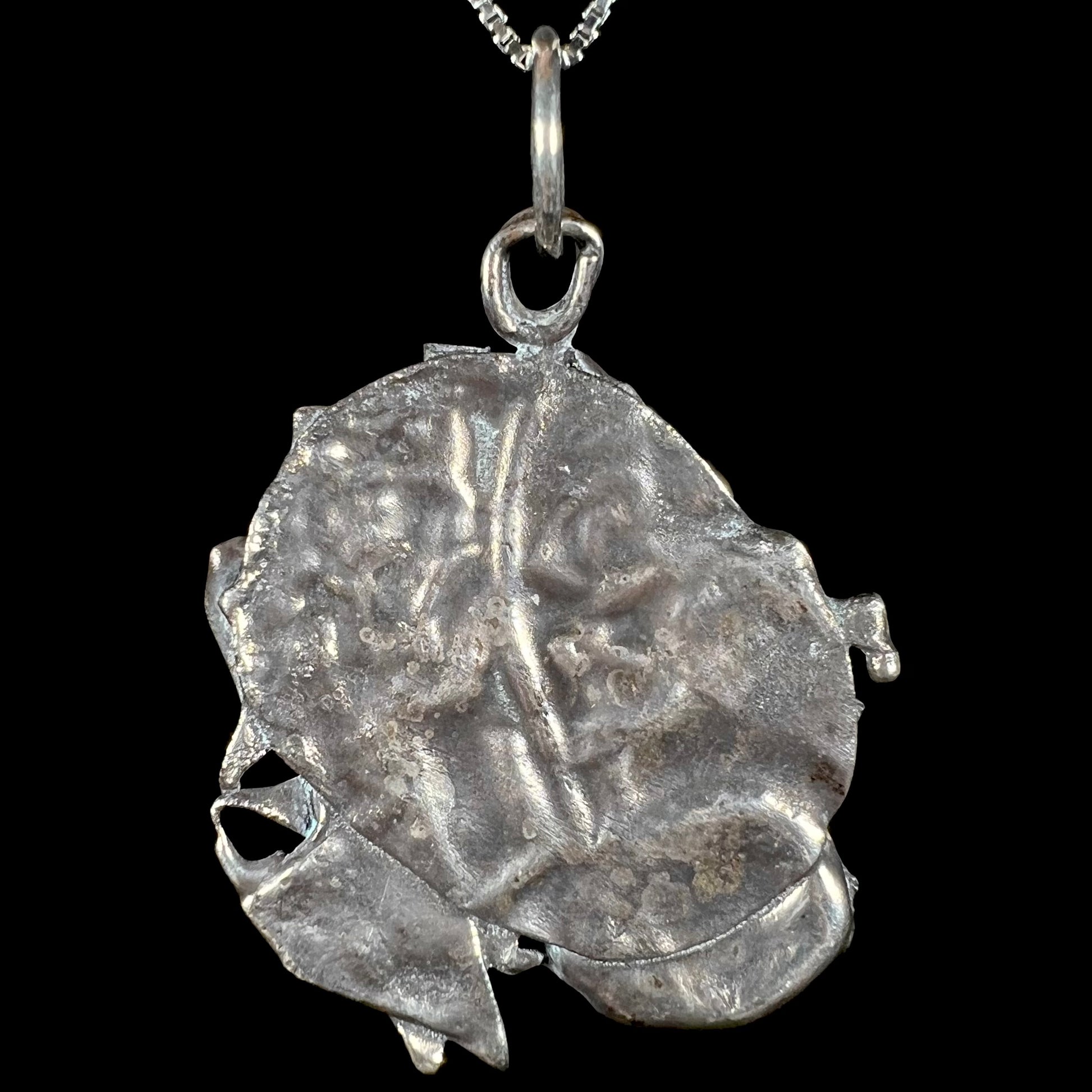 Back view of a brutalist sterling silver pendant against a black background.