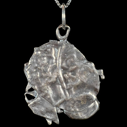 Back view of a brutalist sterling silver pendant against a black background.
