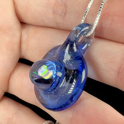 A domed blue glass pendant hand-blown by Michigan artist, Cameron Scott, shown from an angle close-up in a hand.