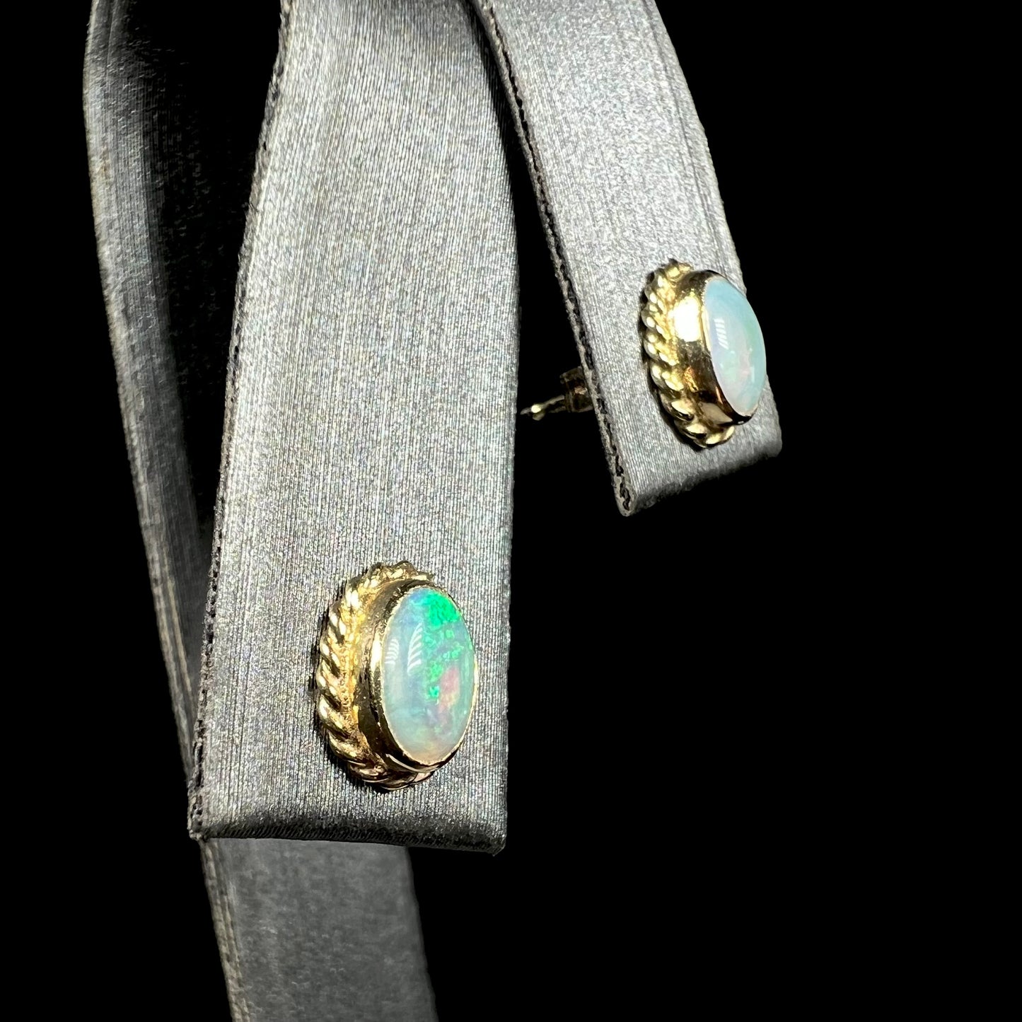 Carla brand yellow gold opal stud earrings with rope design shown from angled view on earring display against black backdrop.