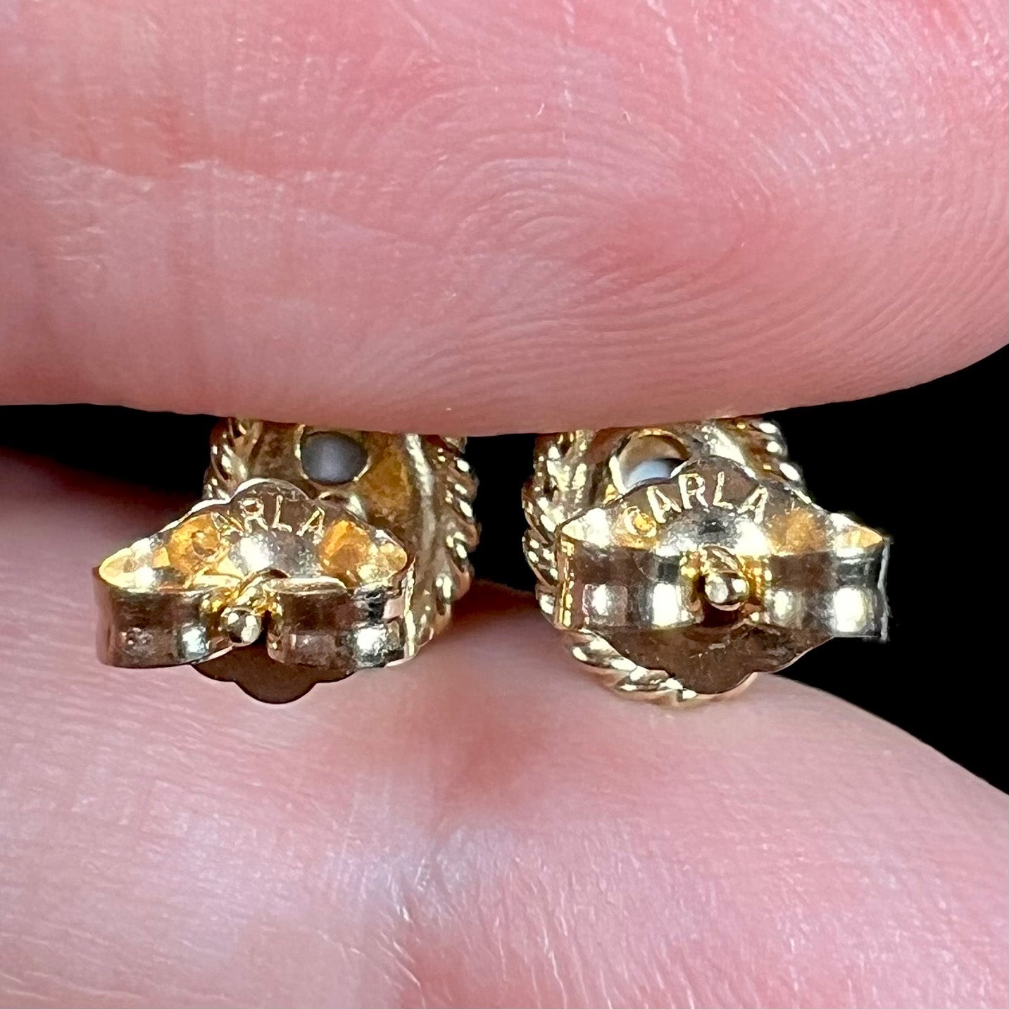 Macro view of gold earring backs engraved "CARLA", held between two fingers.