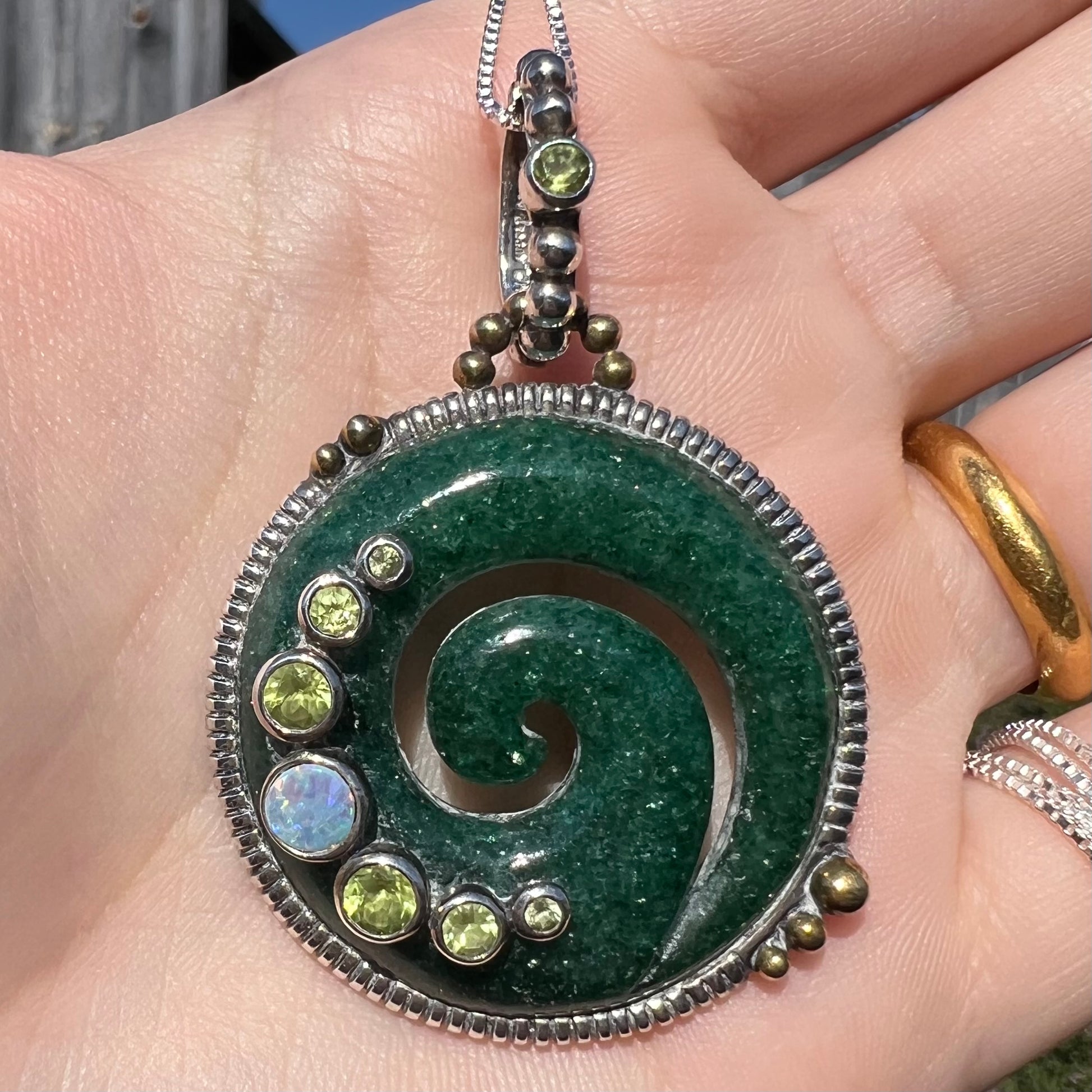 A men's aventurine koru necklace, accented with opal and peridot, shown close-up in sunlight.