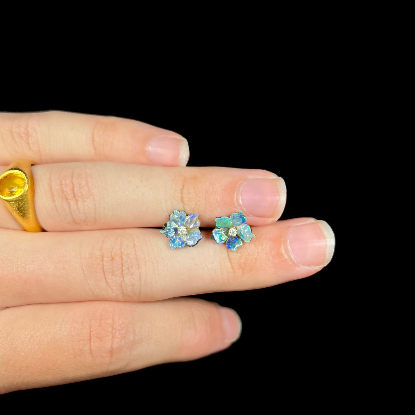A pair of carved boulder opal doublet flower earring jackets with gold CZ studs shown resting on a hand between its fingers.