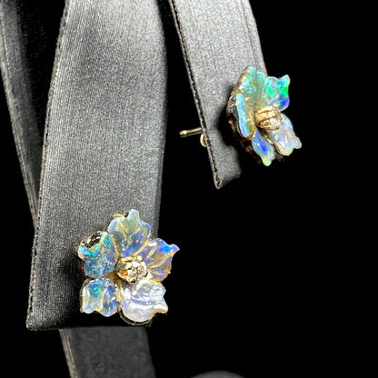 A pair of carved boulder opal doublet flower earring jackets with gold CZ studs shown on an earring display from an angle.