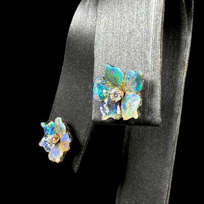 Angled view of a pair of carved boulder opal doublet flower earring jackets with gold CZ studs shown close-up on an earring display.