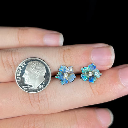 A pair of carved boulder opal doublet flower earring jackets with gold CZ studs shown next to a dime coin, resting on a hand.