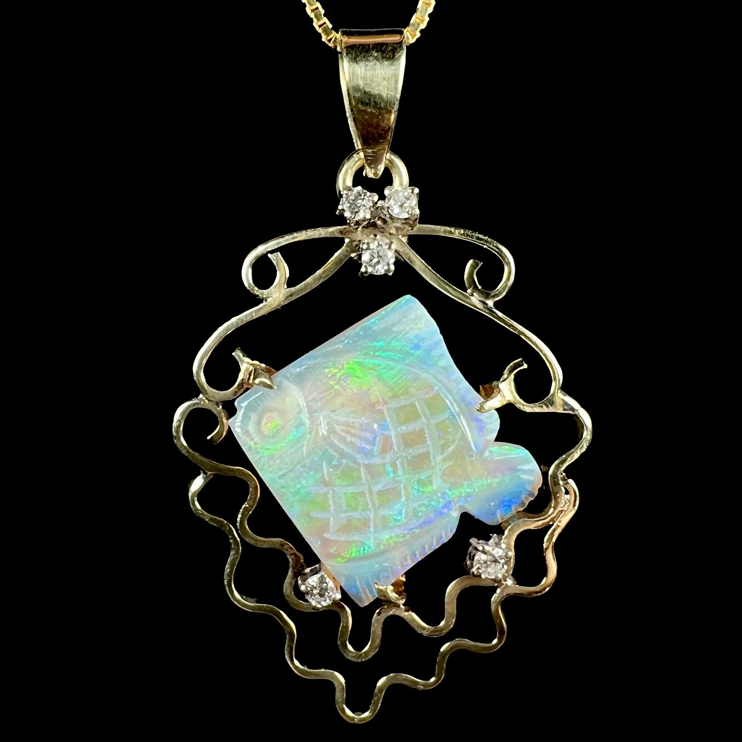Close-up of an ocean-inspired carved opal fish and diamond-accented pendant in 14k gold