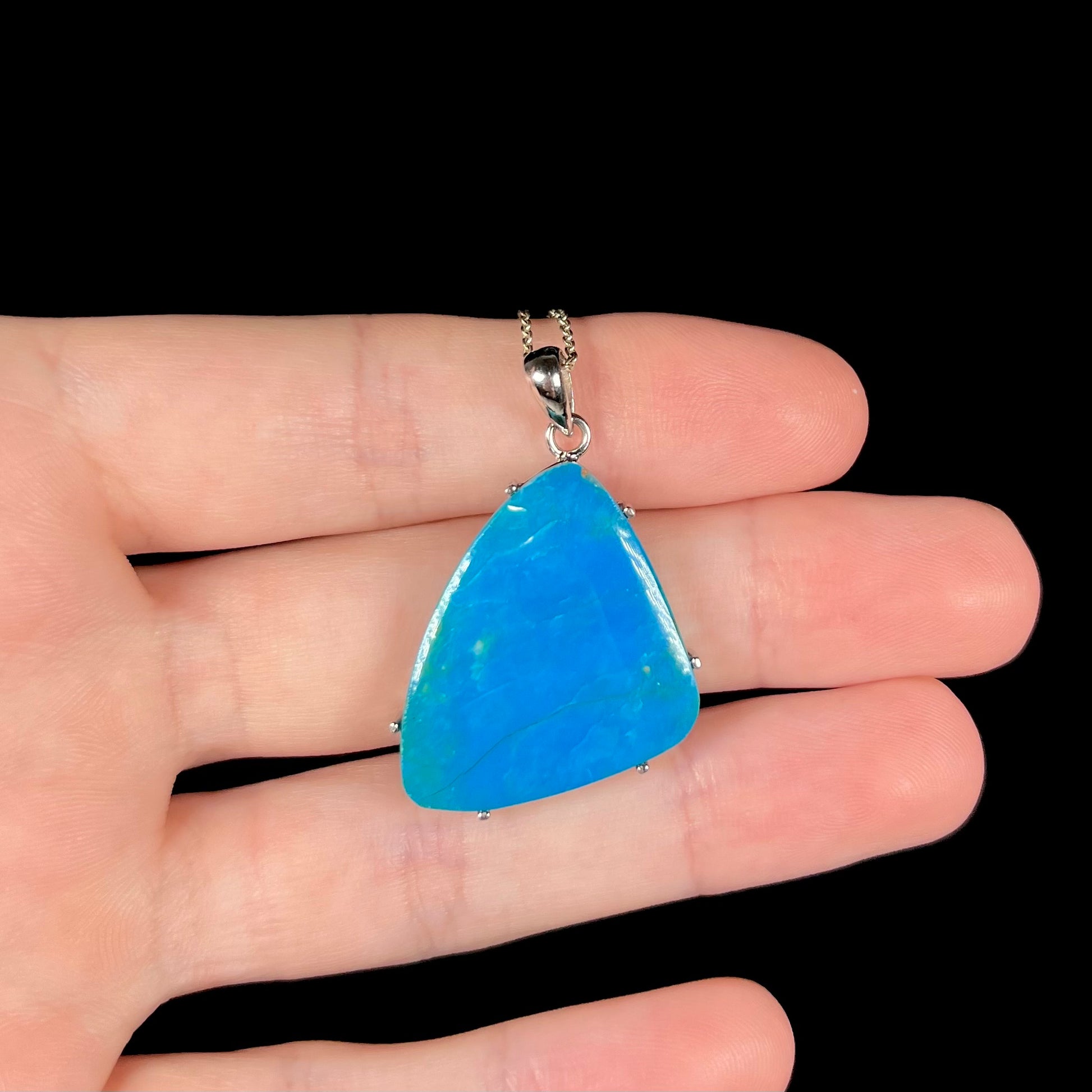 A Chilean blue opal necklace resting on fingers against a black background.