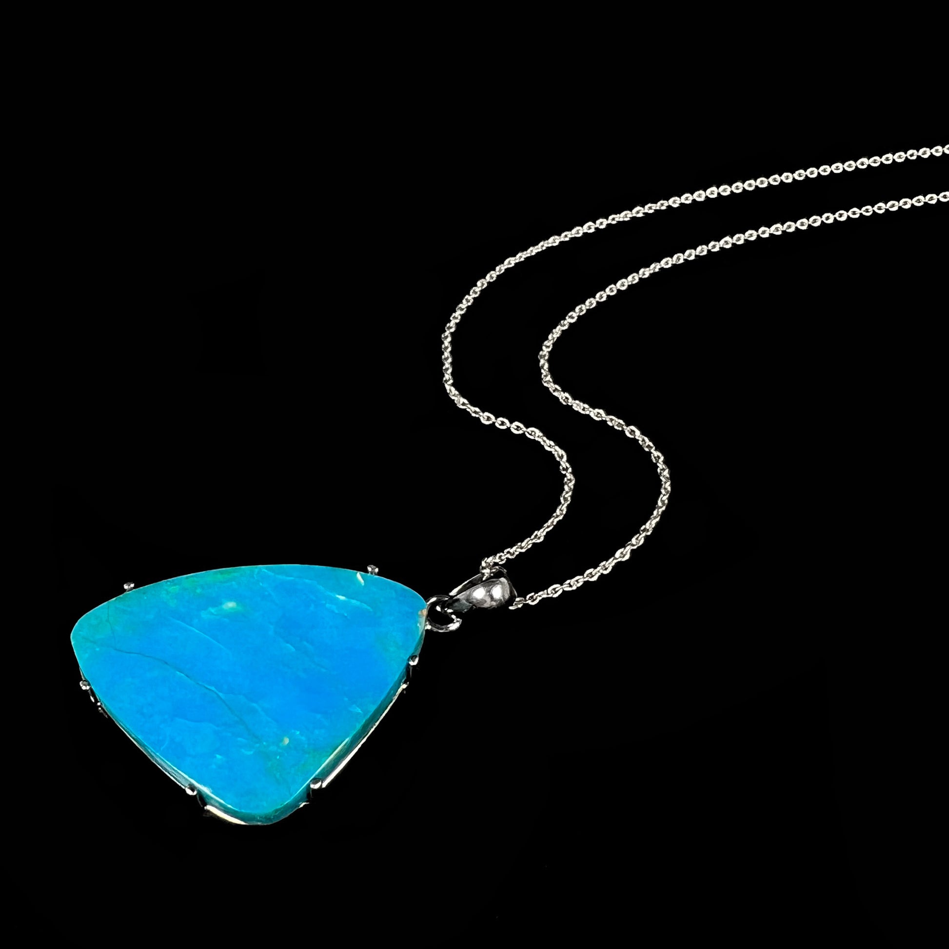 An angled view of a Chilean opal necklace lying on a black background, showing its vibrant turquoise-blue color.