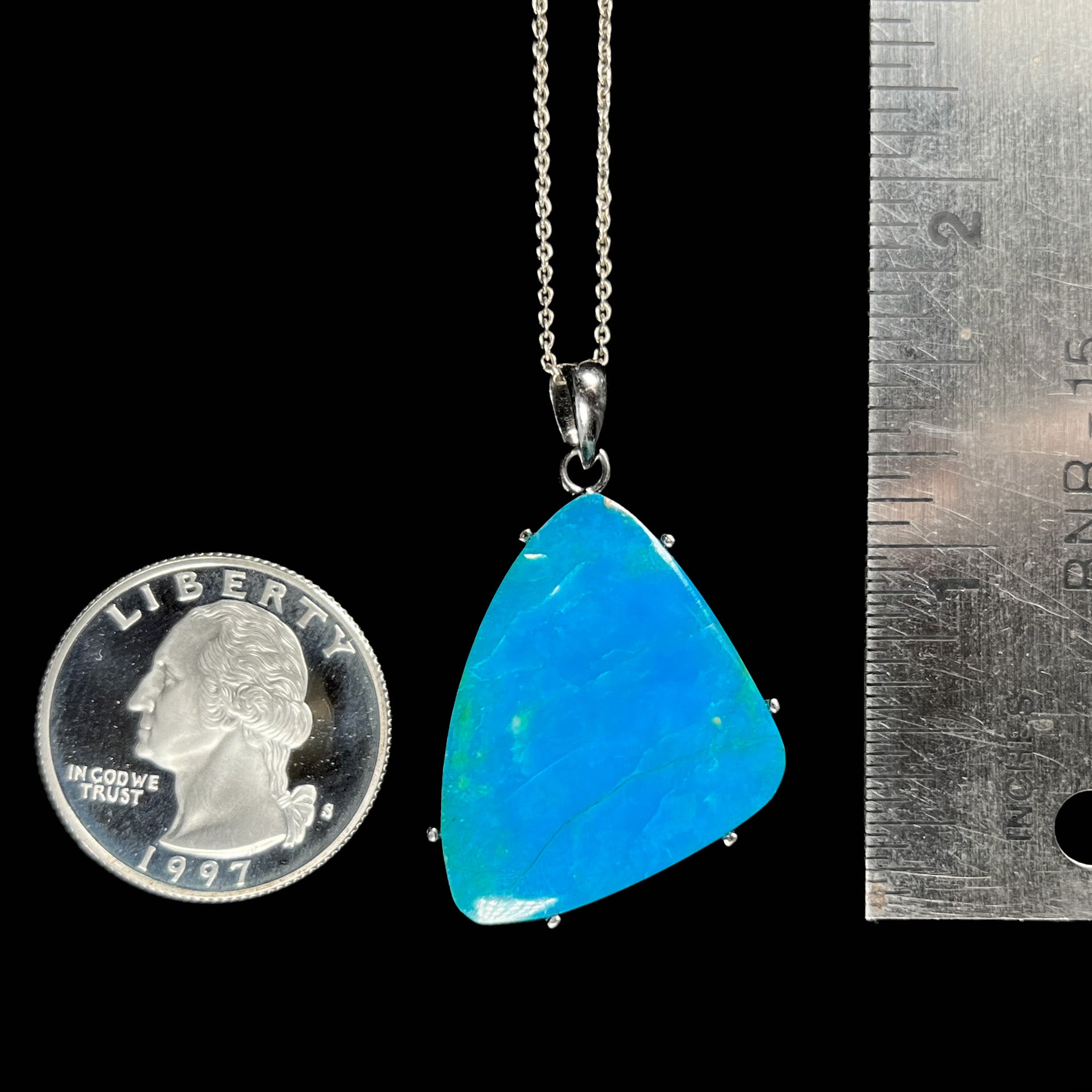 A Chilean opal necklace next to a quarter and ruler for size comparison, measuring approximately 1.5 inches with the bail.