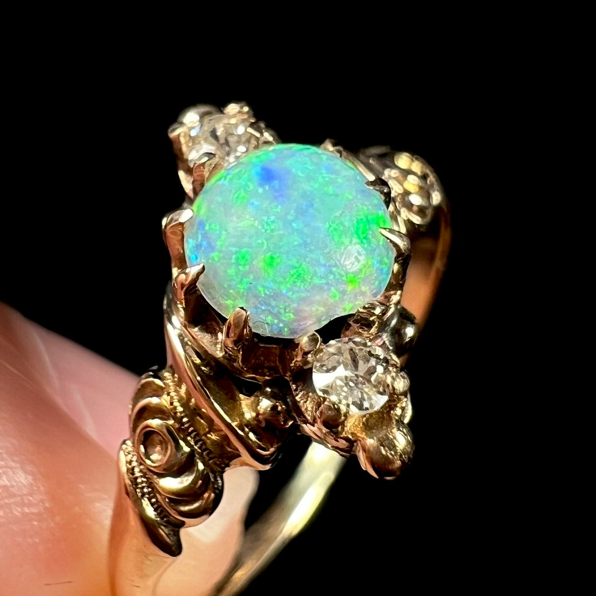 Close-up macro view of chip on edge of round Austrailan opal mounted in antique gold Art Nouveau ring; damage is also seen on prongs holding the opal and Old European Cut accent diamond