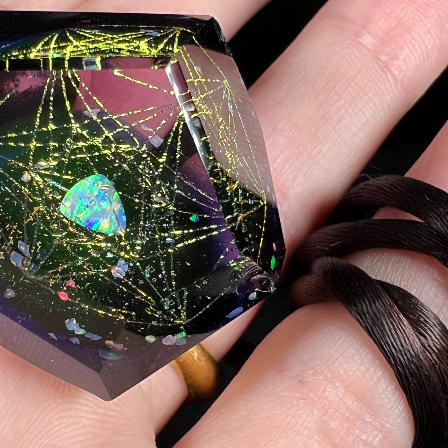 A chipped facet shown on a lab-created opal in glass pendant, shown in a hand.