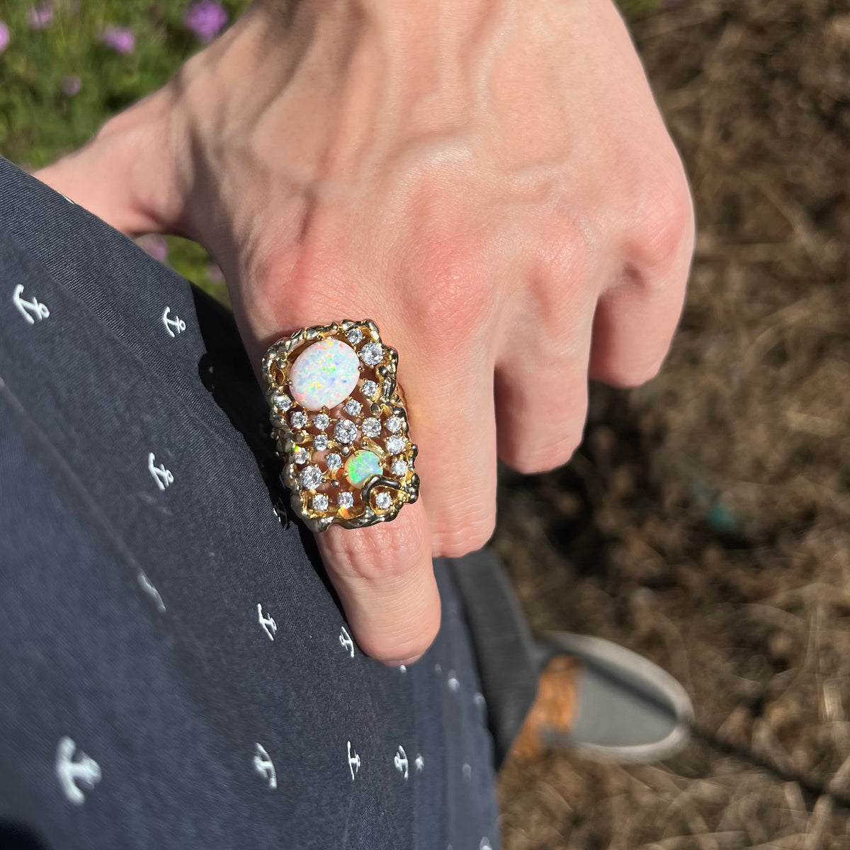 Person's hand resting on hip in natural light wearing a chunky men's costume ring set with two lab-created opals and CZs in gold-plated base metal.