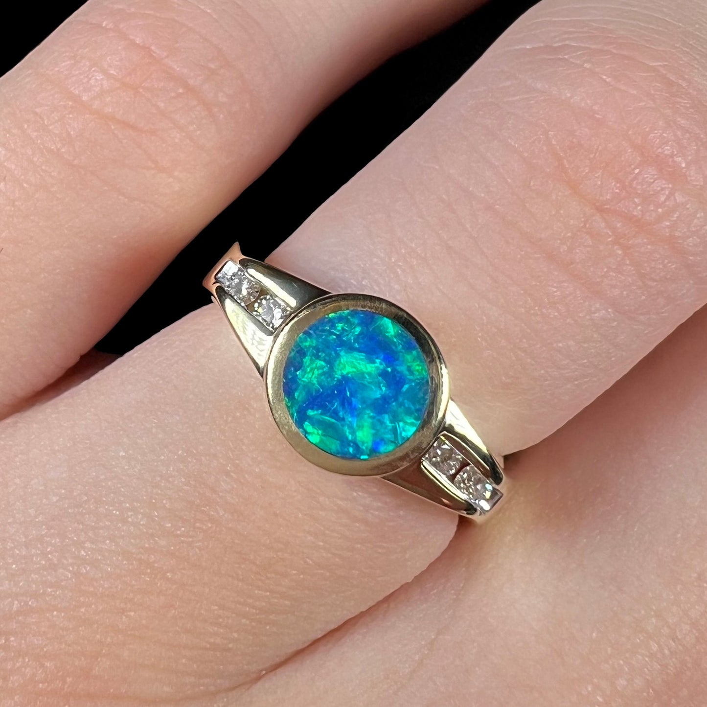 A clean-face Australian boulder opal ring with green color play over an N4 black body tone, shown close-up on a finger.