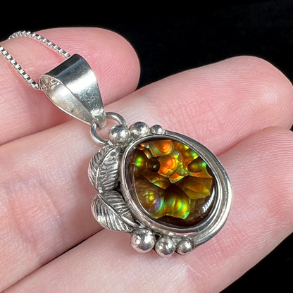 Angled close-up of a colorful Mexican fire agate pendant held in a hand.  The fire agate has iridescent orange, green, yellow, and purple botryoidal banding.