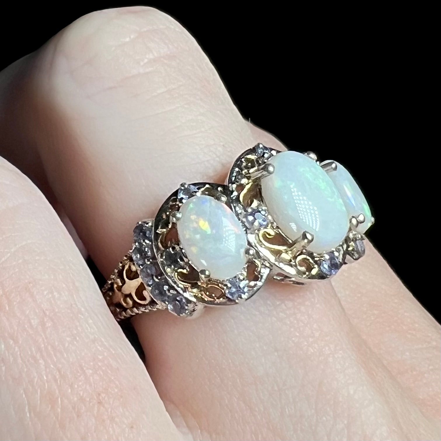Finger wearing a Coober Pedy, Australian opal and tanzanite ring made from sterling silver with gold-tone open filigree details.