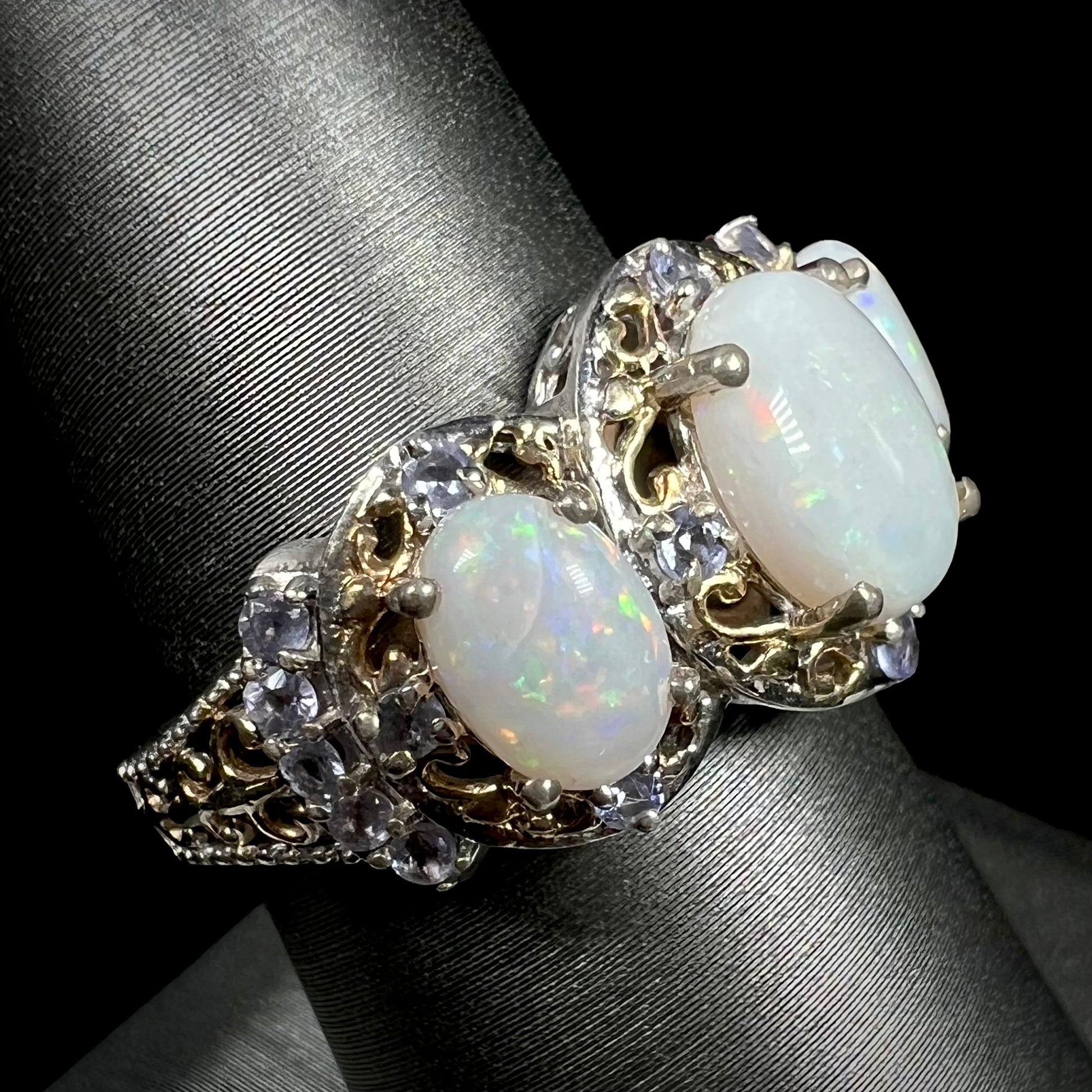 Angled close-up of a Coober Pedy, Australian opal and tanzanite ring shown on a ring display.  One of the opals has an eye-visible crack inclusion.